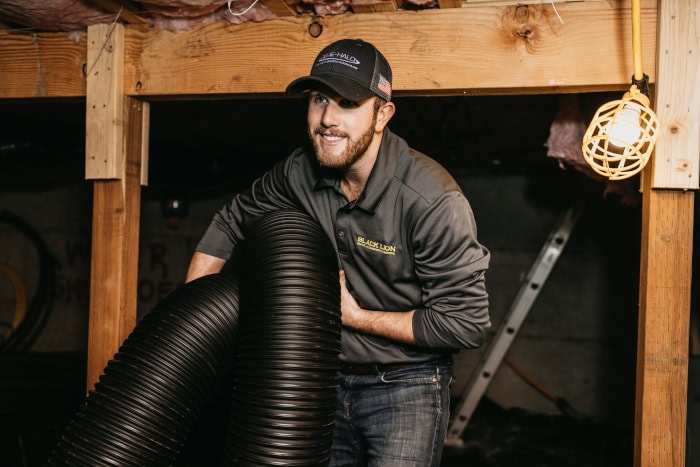 Black Lion HVAC technician walking away from attic holding tubing.
