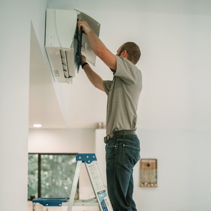Black Lion HVAC technician on a ladder checking ceiling ductless system.