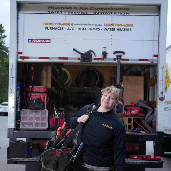 Black Lion HVAC technician holding tools outside of branded work truck.