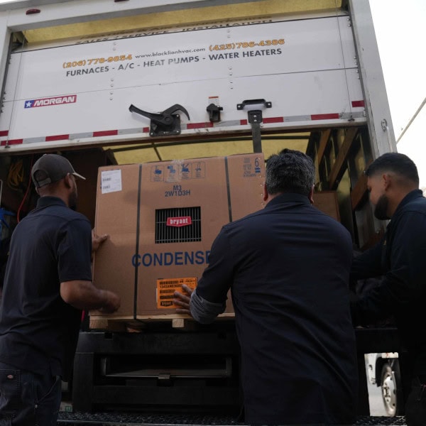 Three Black Lion HVAC technicians removing air conditioner from back of branded work truck.