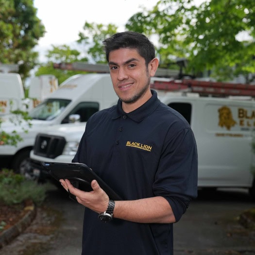 Black Lion HVAC technician standing in front of 3 branded work trucks.