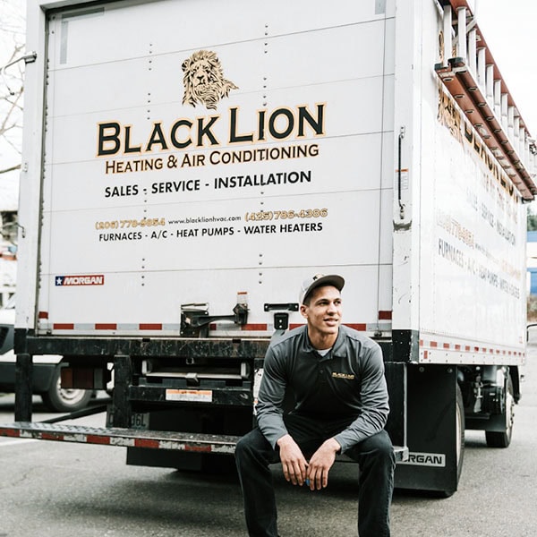 Black Lion HVAC technician sitting on back of company van.