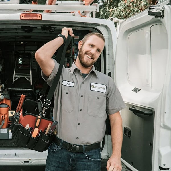 Black Lion Heating, Air Conditioning, & Electrical technician with a tool bag walking away from the back of the company truck.
