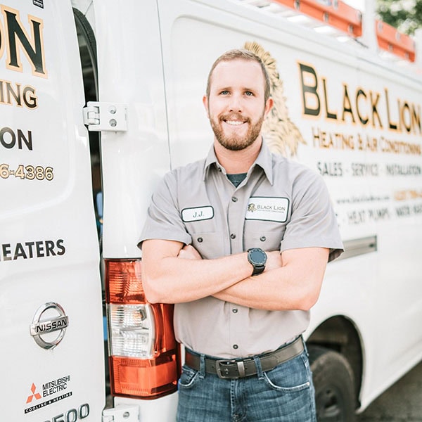 Black Lion Heating, Air Conditioning, & Electrical technician standing and smiling in front of company truck.