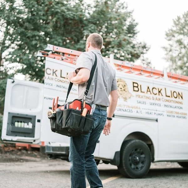 Black Lion Heating, Air Conditioning, & Electrical technician walking back to the company truck holding a tool bag.