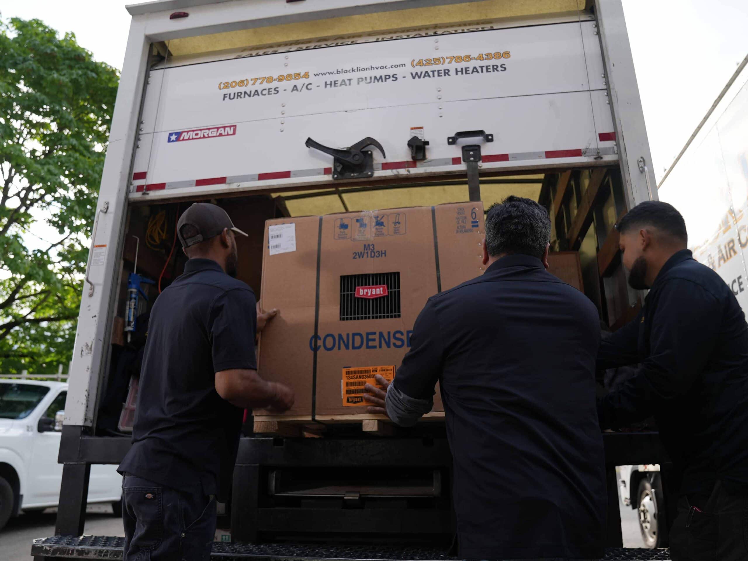Three Black Lion HVAC technicians removing air conditioner from back of branded work truck.