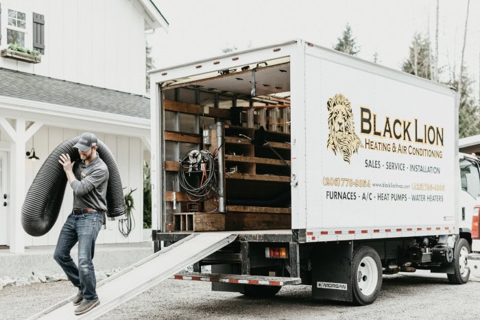 Black Lion HVAC technician walking away from branded work truck, holding tubing.