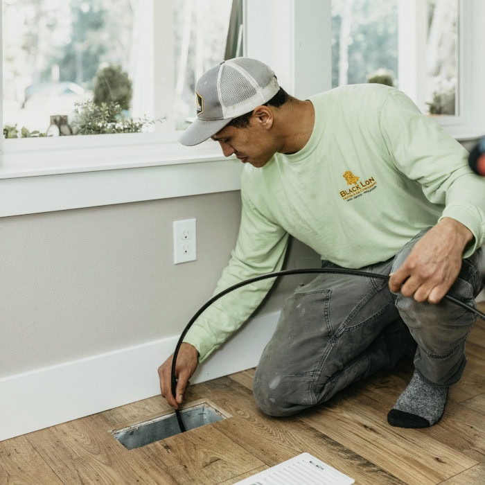 Black Lion HVAC technician checking inside of floor vent.