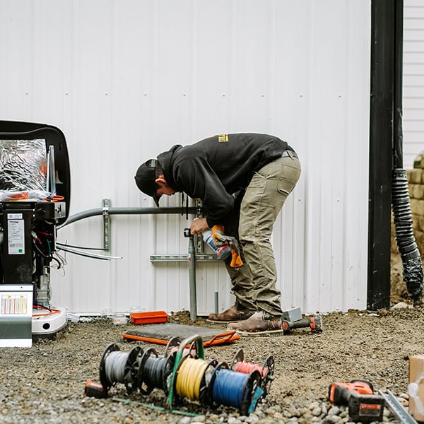 Black Lion Heating, Air Conditioning, & Electrical technician installing a whole-house generator next to a house.